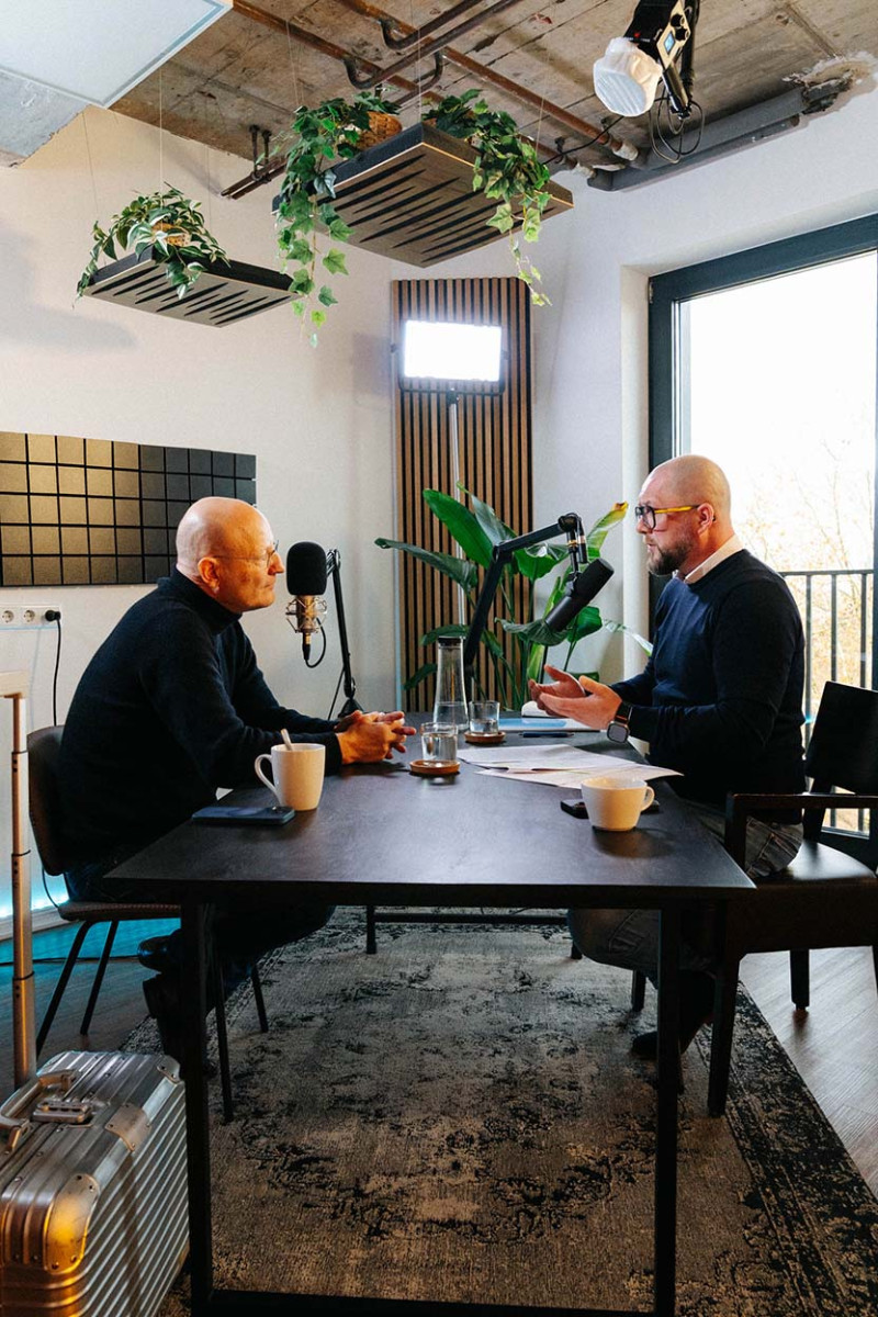 Zwei Gesprächspartner am Aufnahmetisch, dazwischen Mikrofone und Kaffeetassen