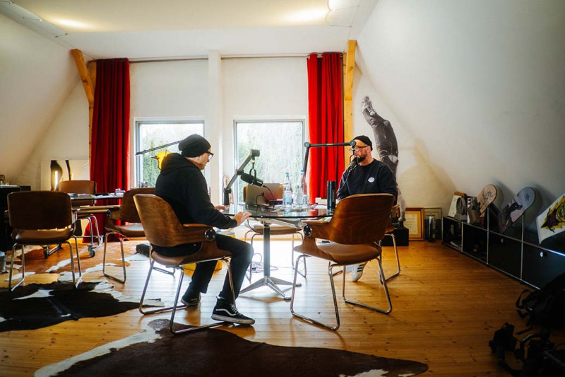 Aufnahme in einem Dachgeschoss mit roten Vorhängen, an der Wand hängen Skateboards